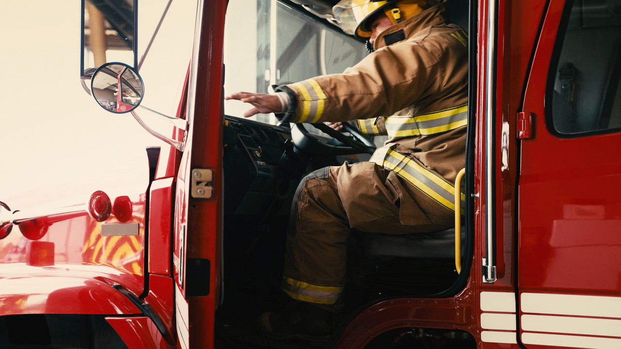 Brandman sitter i förarsätet på en brandbil och håller på att stänga dörren.